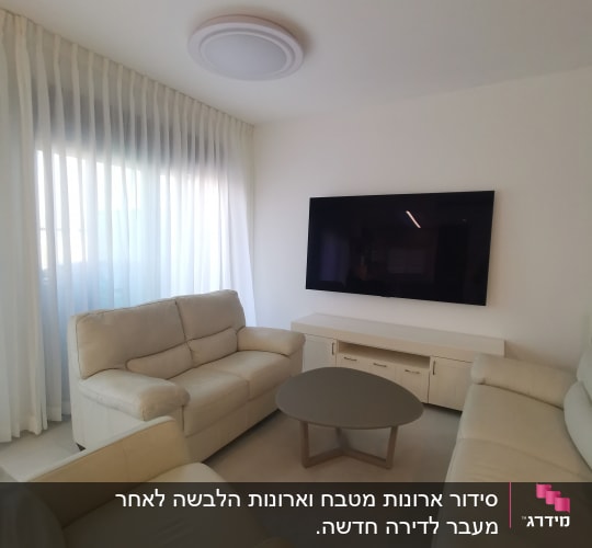 סלון עם ספות בהירות, שולחן עגול וטלוויזיה על הקיר.